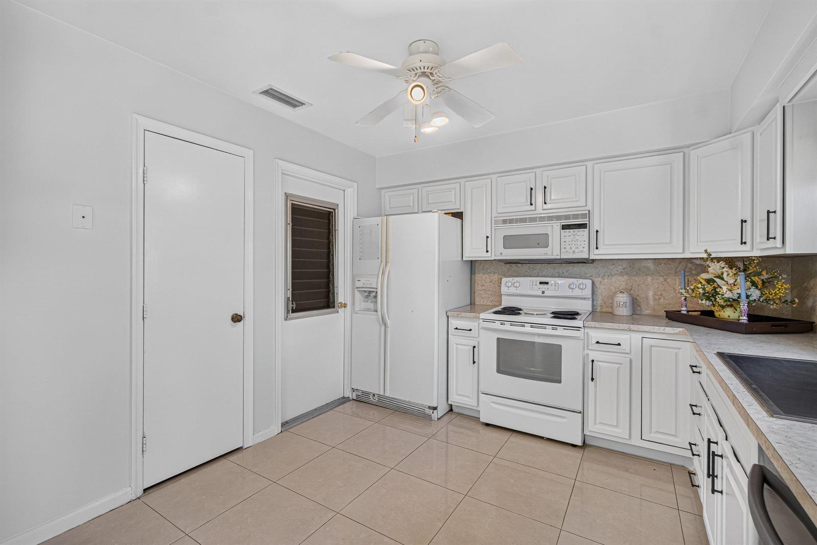 A kitchen features white cabinetry, white appliances, a ceiling fan, and light-colored tile flooring — 9830 Bischofia Tree Way, Boynton Beach FL 33436, BOYNTON BEACH, FL