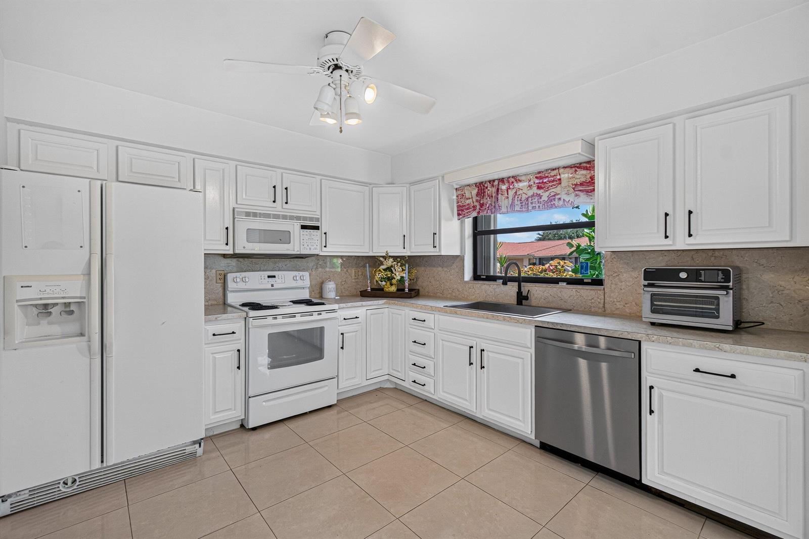A kitchen features white cabinetry, a white stove, a stainless steel dishwasher, and tile flooring — 9830 Bischofia Tree Way, Boynton Beach FL 33436, BOYNTON BEACH, FL