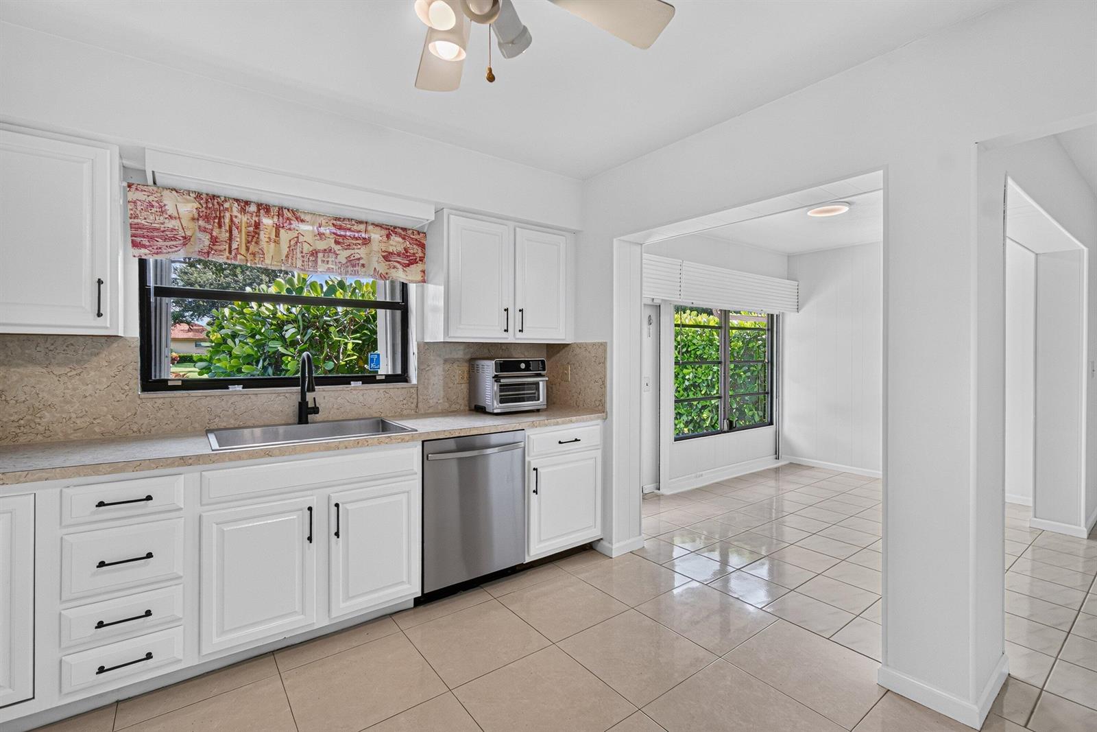 A white kitchen features stainless steel appliances, tile flooring, and an adjacent dining area — 9830 Bischofia Tree Way, Boynton Beach FL 33436, BOYNTON BEACH, FL