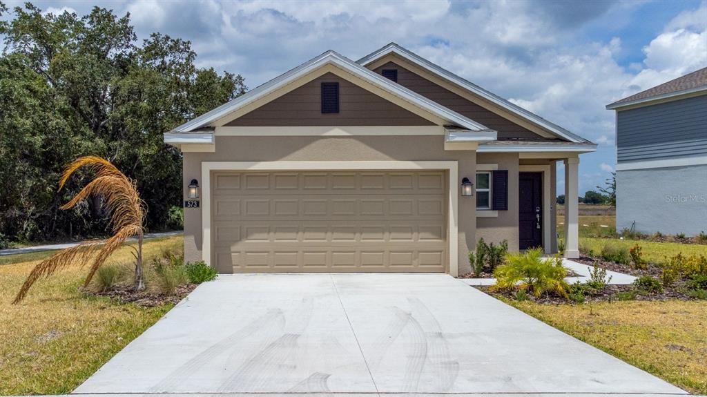 A single-story house with a tan stucco exterior, a two-car garage, and a concrete driveway — 573 BELL PRAIRIE CIRCLE, LAKE WALES, FL