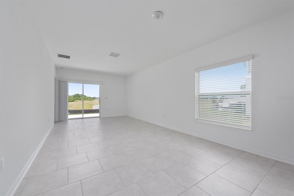 An empty room with white walls, light tile flooring, a window, and a sliding glass door — 573 BELL PRAIRIE CIRCLE, LAKE WALES, FL