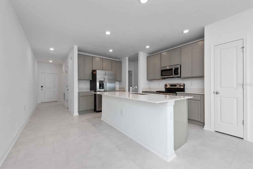A modern kitchen features gray cabinets, stainless steel appliances, and a white quartz island — 573 BELL PRAIRIE CIRCLE, LAKE WALES, FL