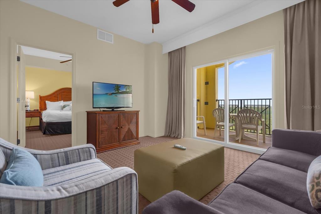 A living room with a television, ottoman, and balcony access, leading into a bedroom — 8101 RESORT VILLAGE DRIVE UNIT 31202, ORLANDO, FL