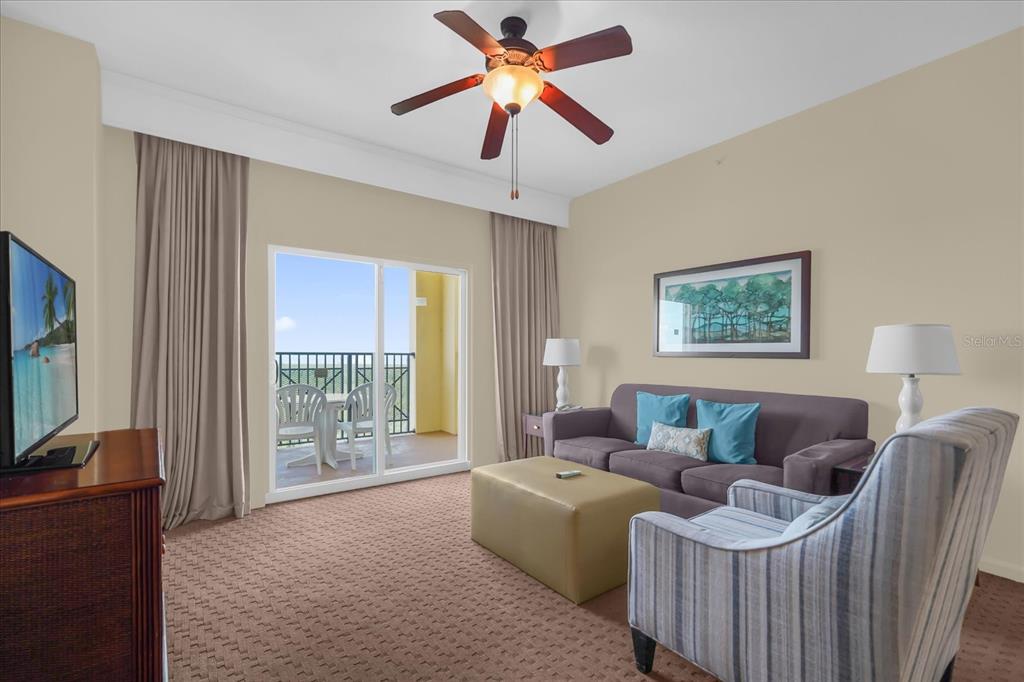 A living room features a sofa, striped armchair, ottoman, ceiling fan, and a balcony view — 8101 RESORT VILLAGE DRIVE UNIT 31202, ORLANDO, FL