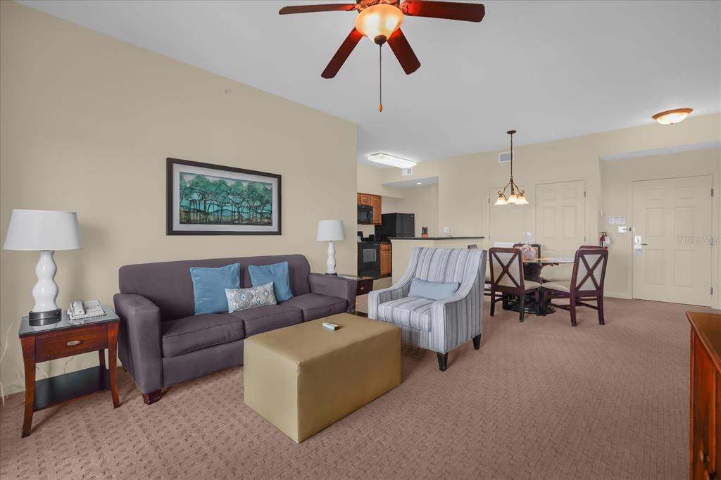 A living room with a sofa, armchair, ottoman, and an adjacent dining area and kitchen — 8101 RESORT VILLAGE DRIVE UNIT 31202, ORLANDO, FL