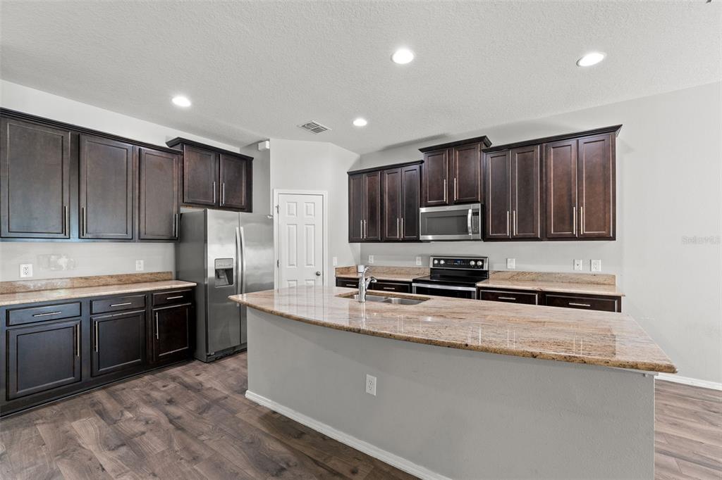 A kitchen features dark wood cabinets, granite countertops, stainless steel appliances, and wood-look flooring — 15531 STONE HOUSE DRIVE, BROOKSVILLE, FL