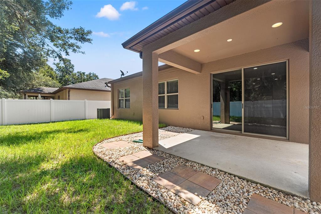 A covered concrete patio with stone pavers overlooks a grassy backyard enclosed by a white fence — 15531 STONE HOUSE DRIVE, BROOKSVILLE, FL