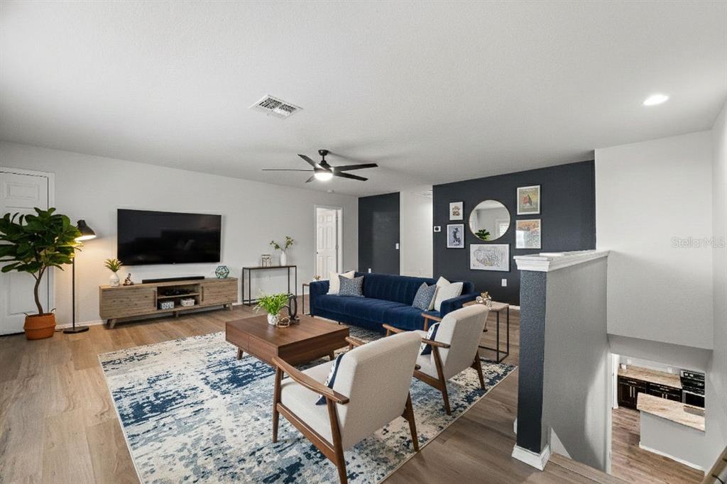 A living room features a blue sofa, two armchairs, a television, and a dark accent wall — 15531 STONE HOUSE DRIVE, BROOKSVILLE, FL
