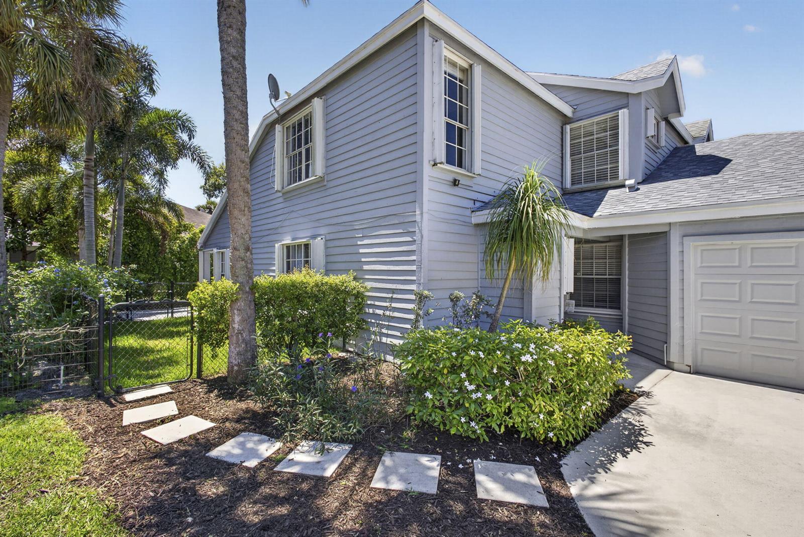 A two-story gray house with a concrete driveway, a small garden, and a chain-link fence — 936 Honeytree Lane # A, Wellington FL 33414, WELLINGTON, FL