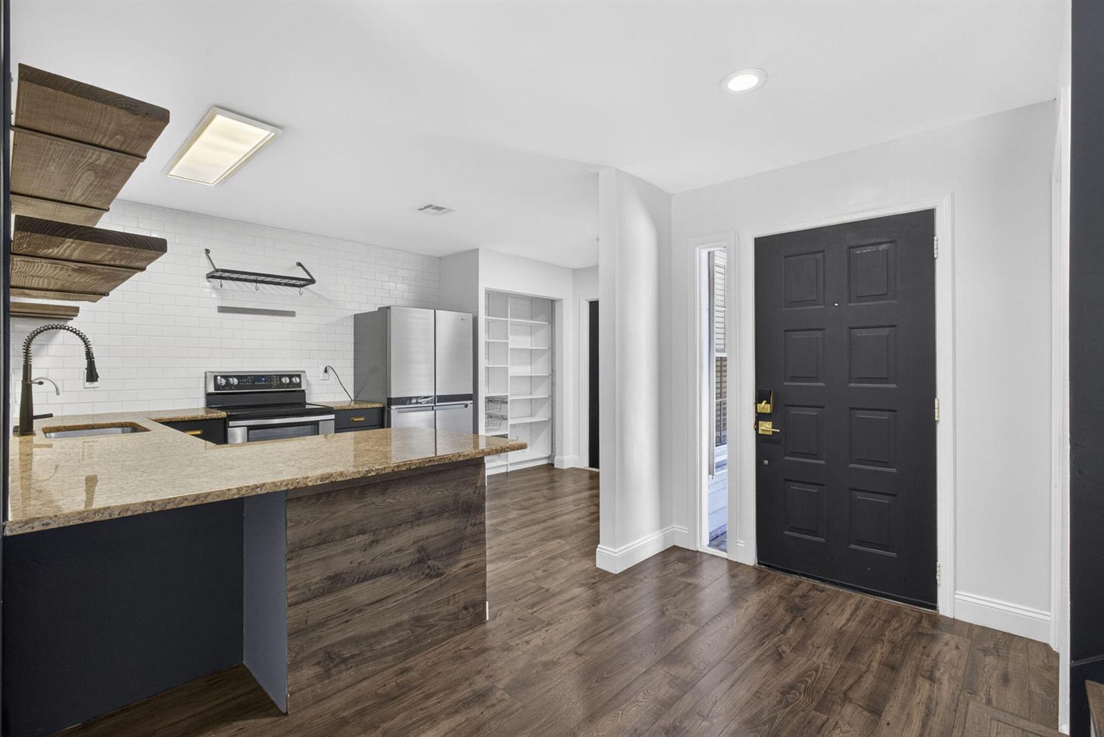 A kitchen features granite countertops, dark cabinetry, open wood shelving, and a black front door — 936 Honeytree Lane # A, Wellington FL 33414, WELLINGTON, FL