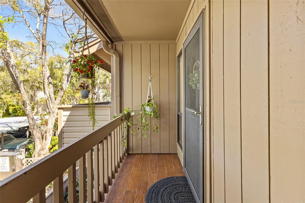A covered balcony features wood-look tile flooring, a wooden railing, and hanging potted plants — 1636 BROOKHOUSE DRIVE UNIT 230, SARASOTA, FL