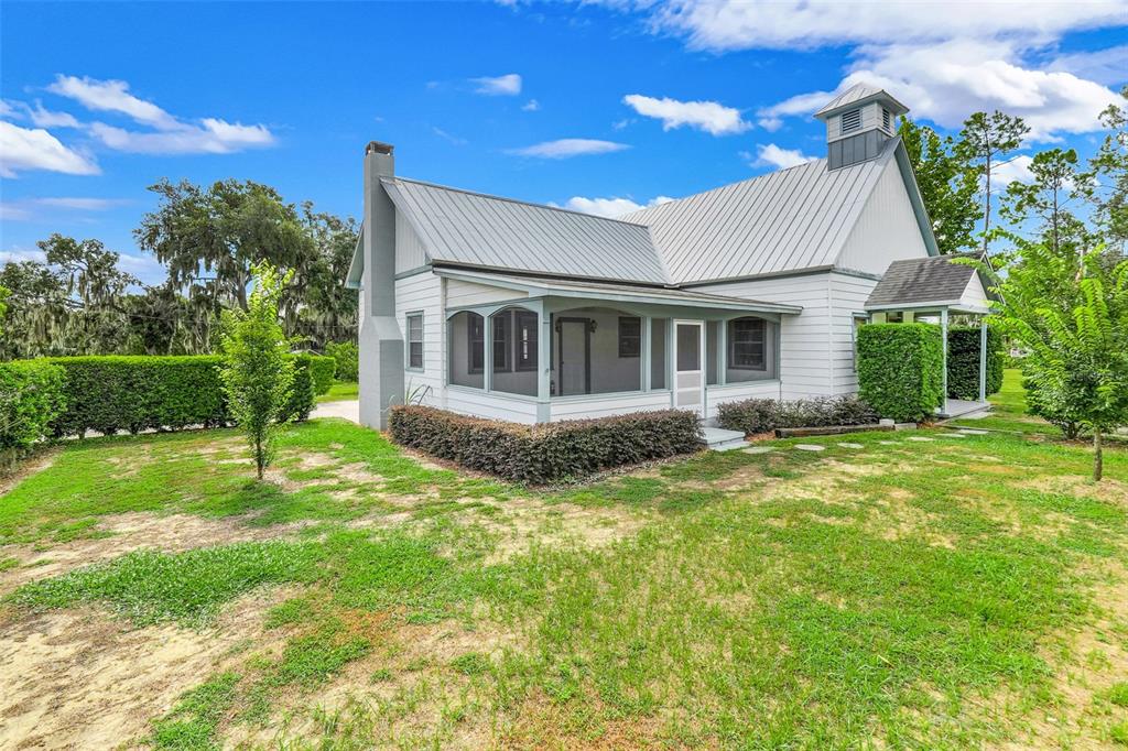 A white house with a metal roof, a screened-in porch, and a chimney sits outdoors — 13234 SOUTH CAROLINA AVENUE, ASTATULA, FL