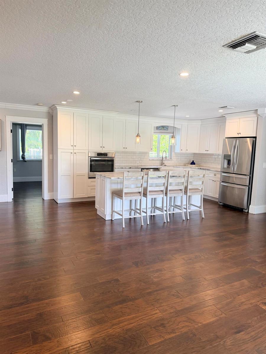 A kitchen features white cabinets, a marble-topped island with four chairs, and dark wood flooring — 401 SE 3rd Terrace, Deerfield Beach FL 33441, DEERFIELD BEACH, FL