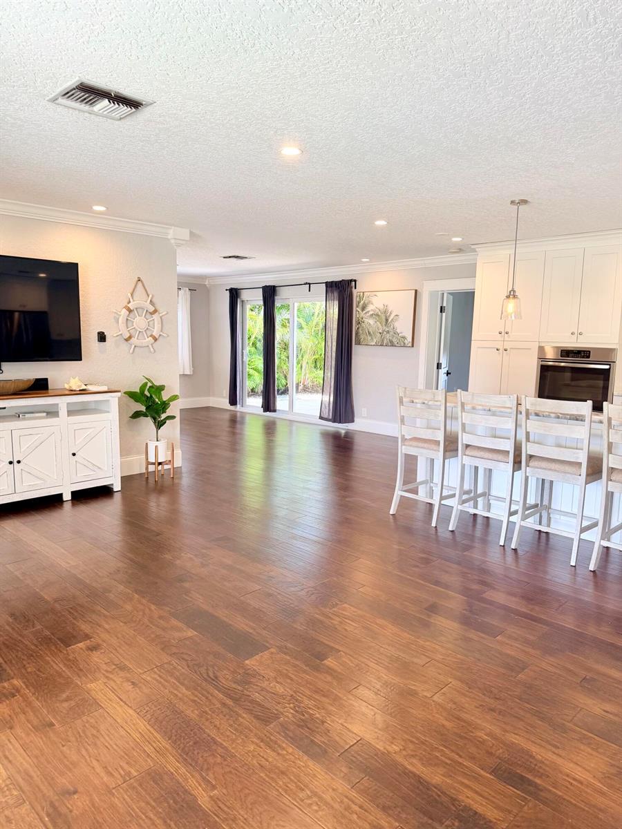 An open-concept living room and kitchen featuring dark wood flooring and white cabinetry — 401 SE 3rd Terrace, Deerfield Beach FL 33441, DEERFIELD BEACH, FL