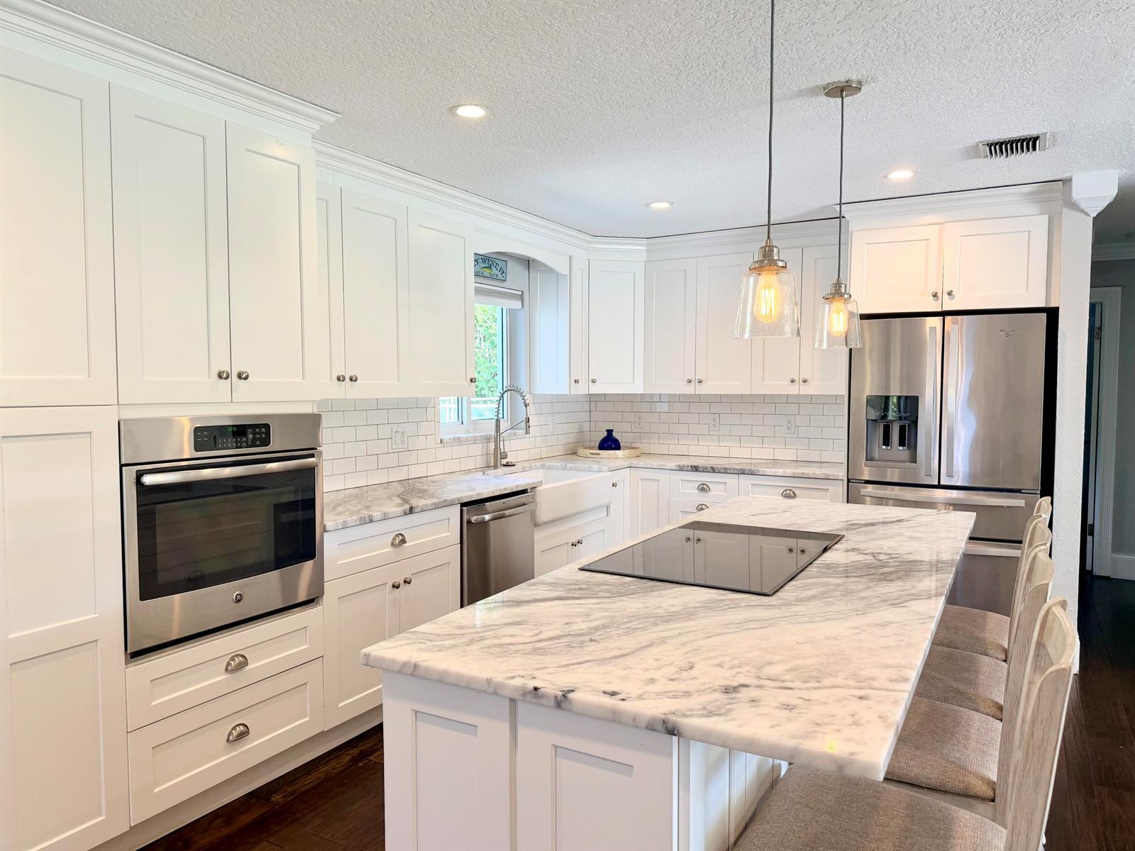 A white kitchen features a marble-topped island, stainless steel appliances, and dark wood flooring — 401 SE 3rd Terrace, Deerfield Beach FL 33441, DEERFIELD BEACH, FL