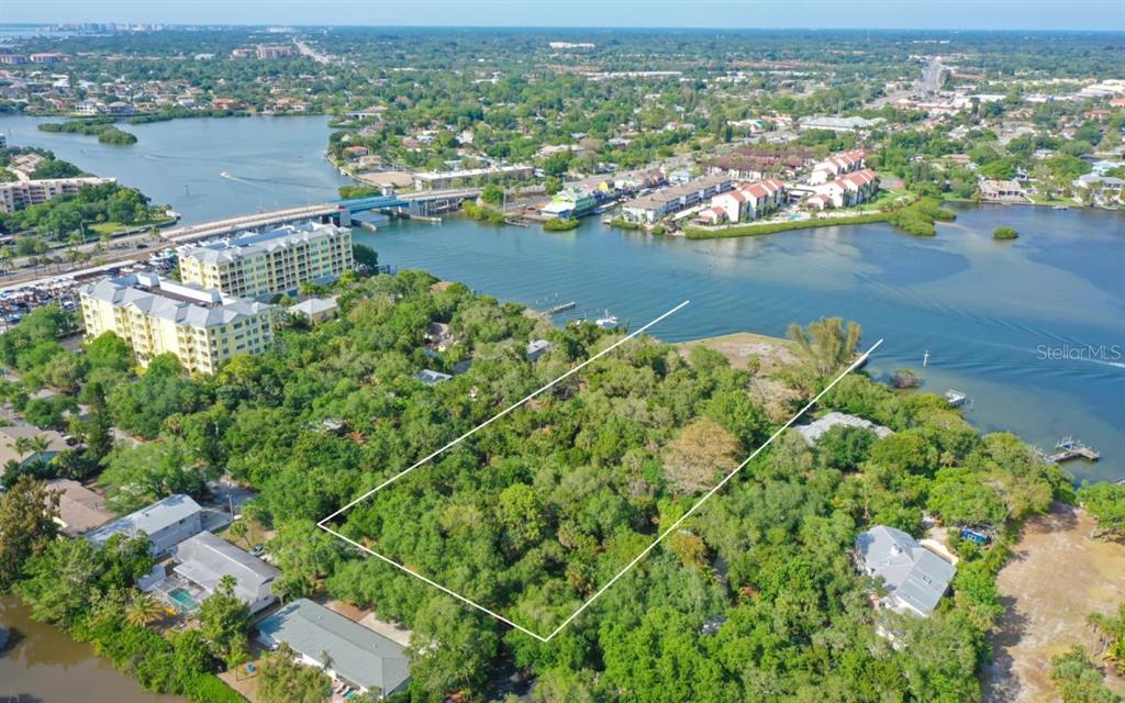 An aerial view shows a wooded, rectangular waterfront lot outlined in white near a bridge — 6559 PEACOCK ROAD, SARASOTA, FL