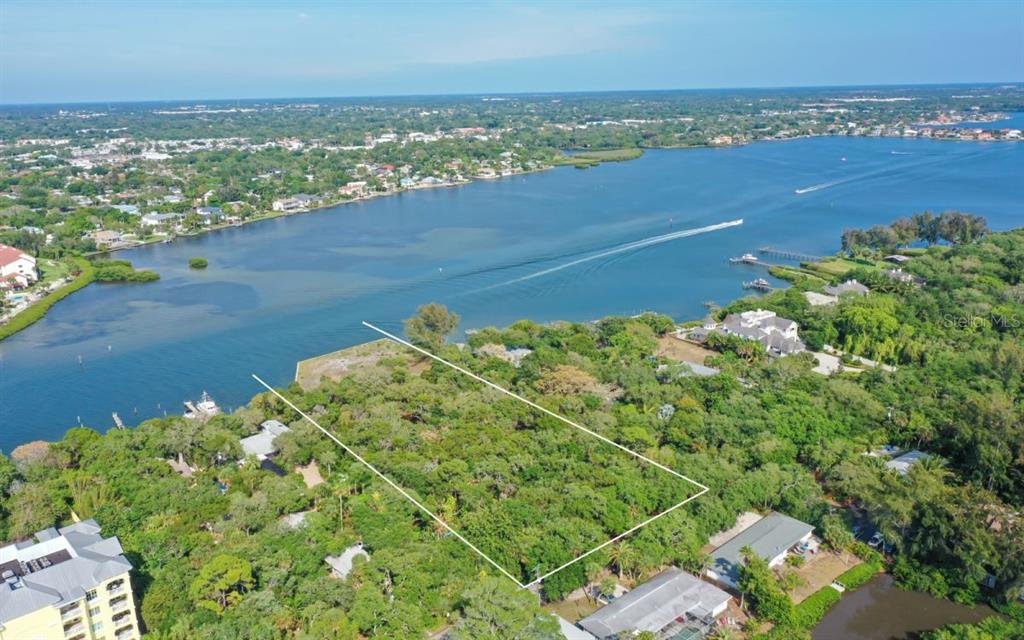 An aerial view shows a rectangular vacant lot surrounded by dense trees near a waterway — 6559 PEACOCK ROAD, SARASOTA, FL