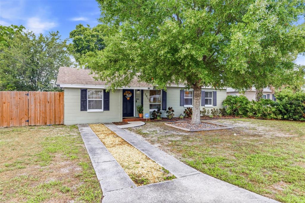 A single-story house with light green siding, a gravel driveway, and a large front tree — 3913 W WALLACE AVENUE, TAMPA, FL