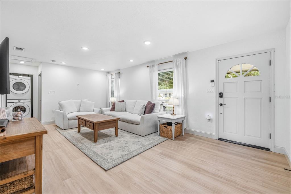 A living room features light wood-look flooring, white walls, a sofa, and a front door — 3913 W WALLACE AVENUE, TAMPA, FL
