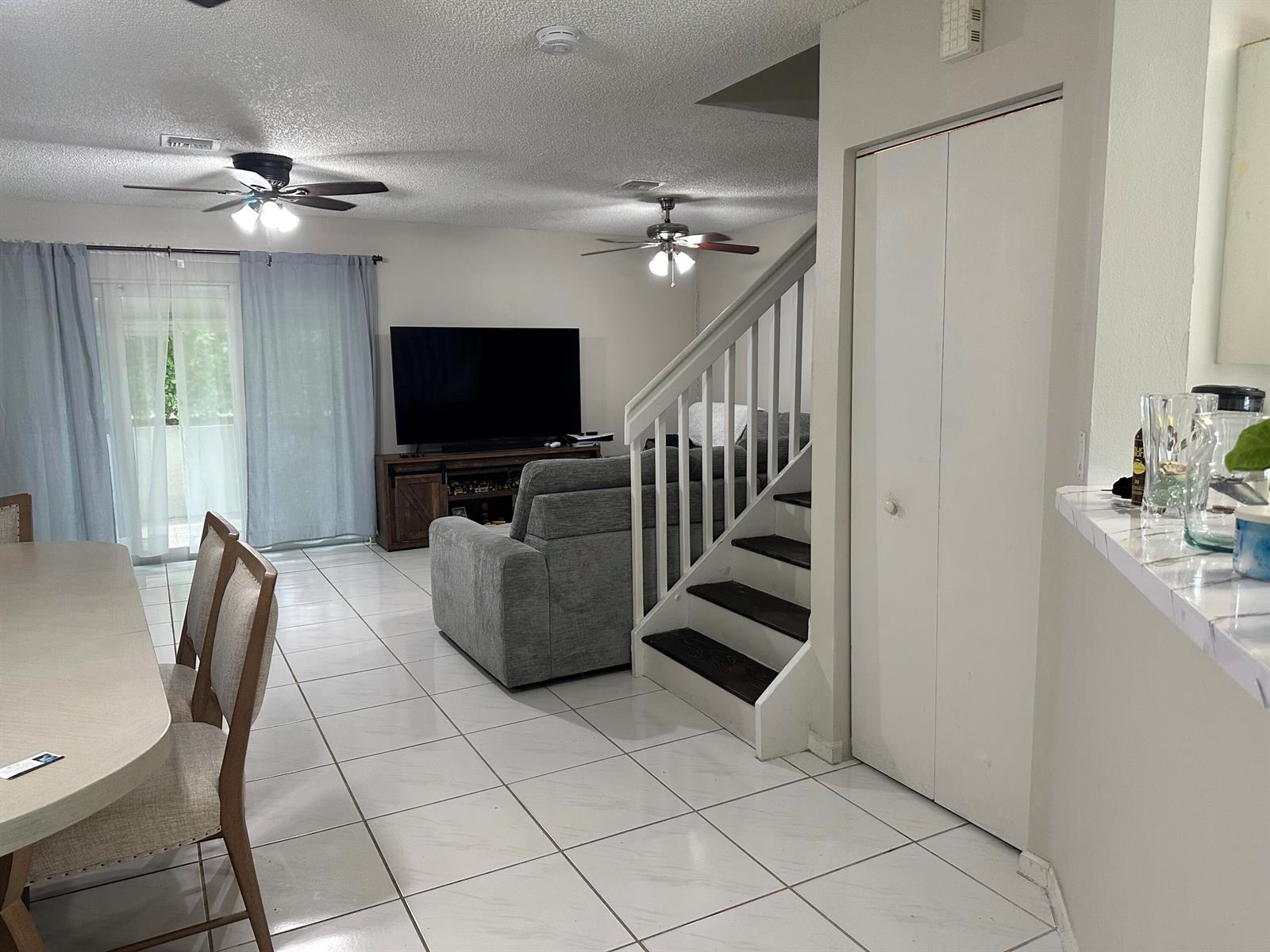 A living room and dining area with white tile floors, a staircase, and ceiling fans — 1420 SW 47TH Avenue, Deerfield Beach FL 33442, DEERFIELD BEACH, FL