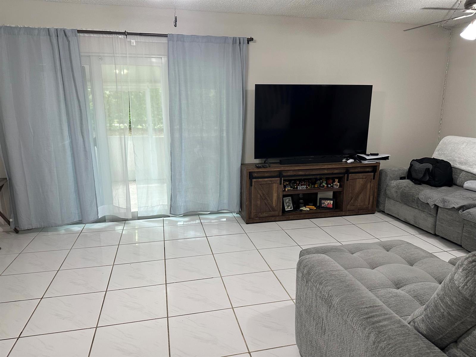 A living room features a large television on a wooden stand, tile flooring, and curtains — 1420 SW 47TH Avenue, Deerfield Beach FL 33442, DEERFIELD BEACH, FL