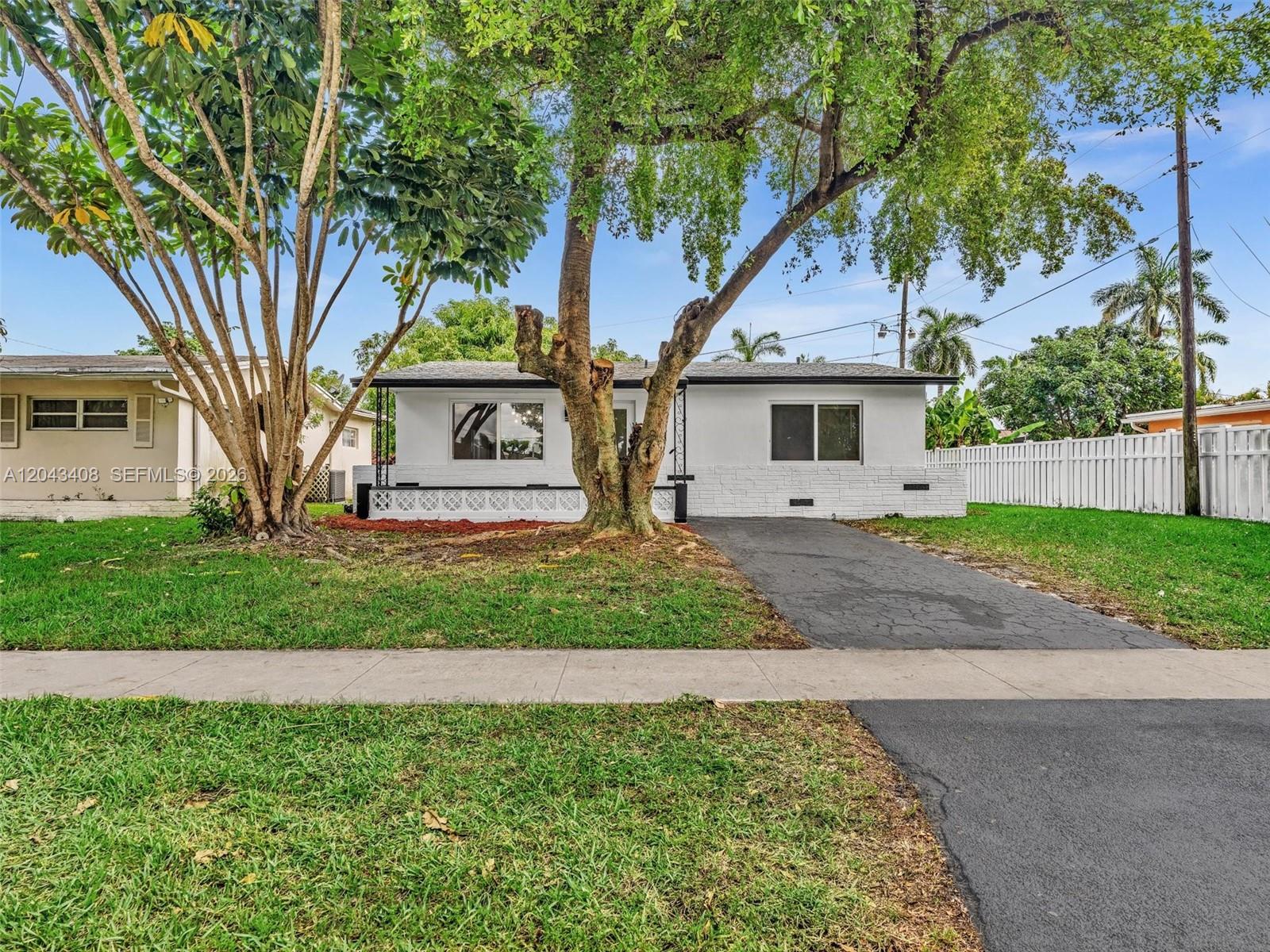 A single-story white house features a paved driveway, a large tree, and a front lawn — 8145 Sunset Strip, Sunrise FL 33322, SUNRISE, FL