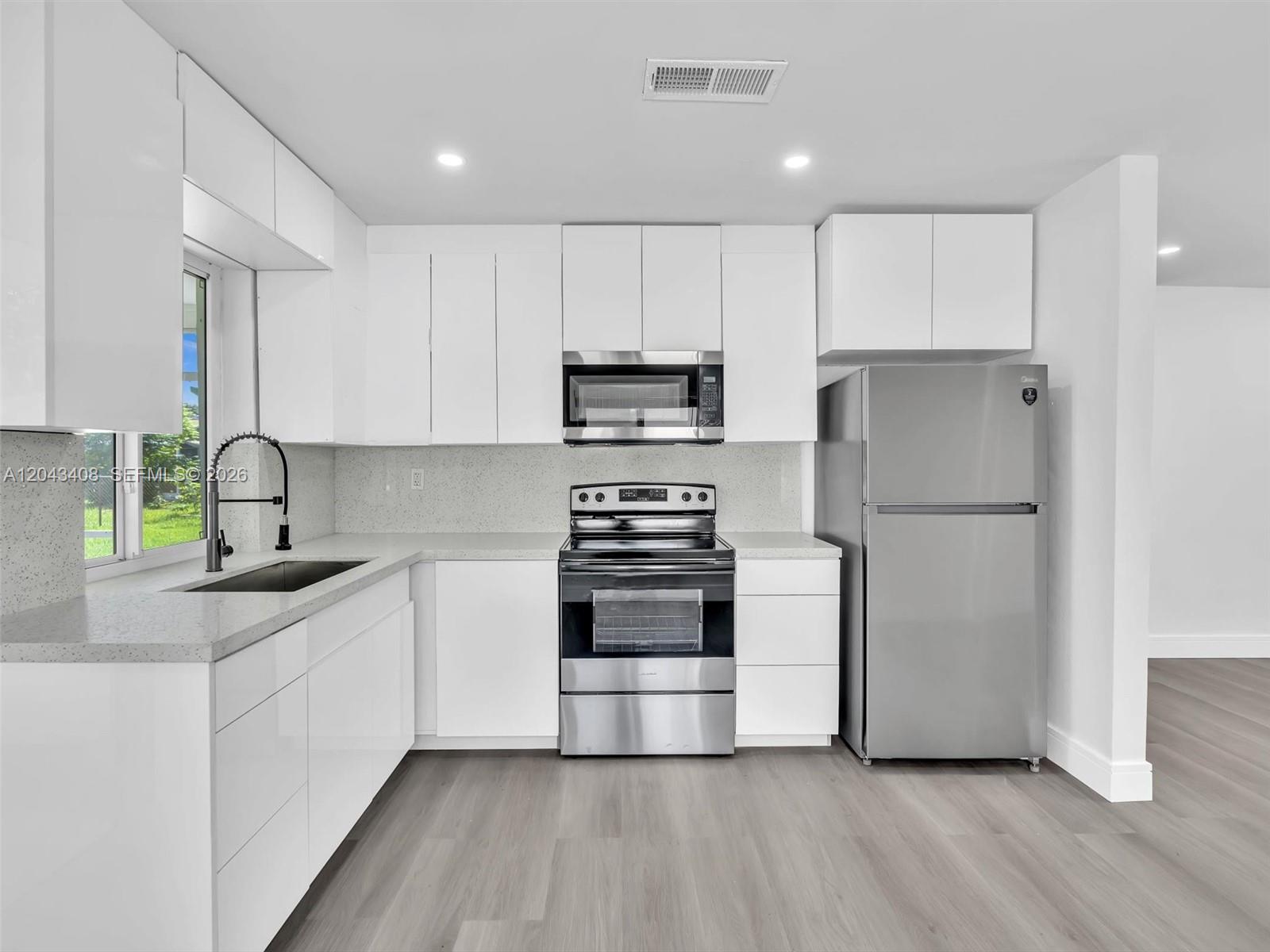 A modern kitchen features white cabinets, stainless steel appliances, and light gray wood-look flooring — 8145 Sunset Strip, Sunrise FL 33322, SUNRISE, FL
