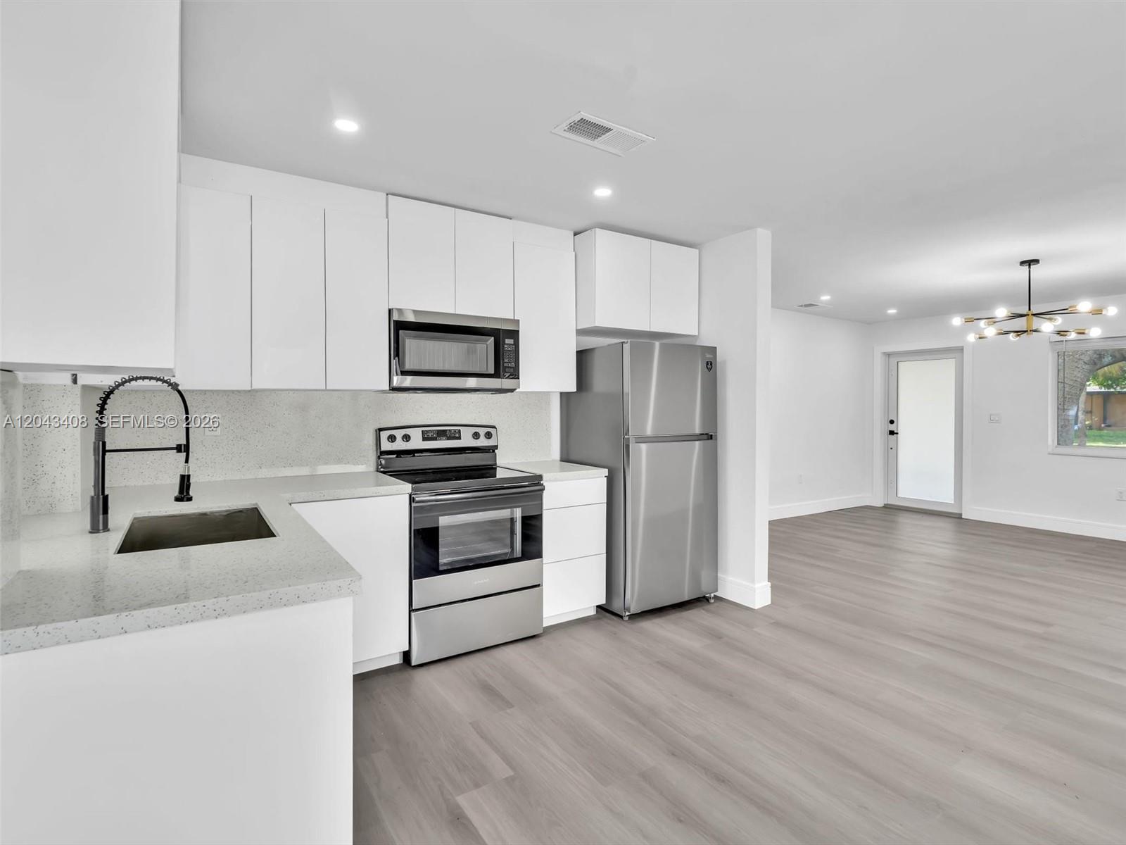A modern kitchen features white cabinetry, stainless steel appliances, and light wood-look flooring — 8145 Sunset Strip, Sunrise FL 33322, SUNRISE, FL