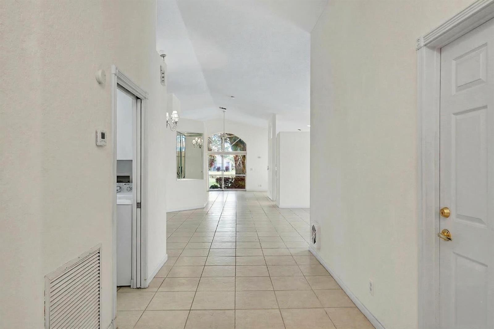 A tiled hallway leads toward a bright living area with vaulted ceilings and a glass door — 10382 Utopia Circle E, Boynton Beach FL 33437, BOYNTON BEACH, FL