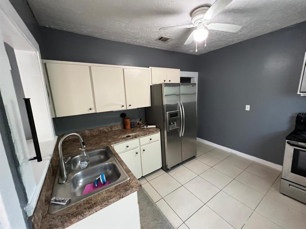 A kitchen features white cabinets, a stainless steel refrigerator, a double sink, and tiled floors — 1708 E NOME STREET, TAMPA, FL