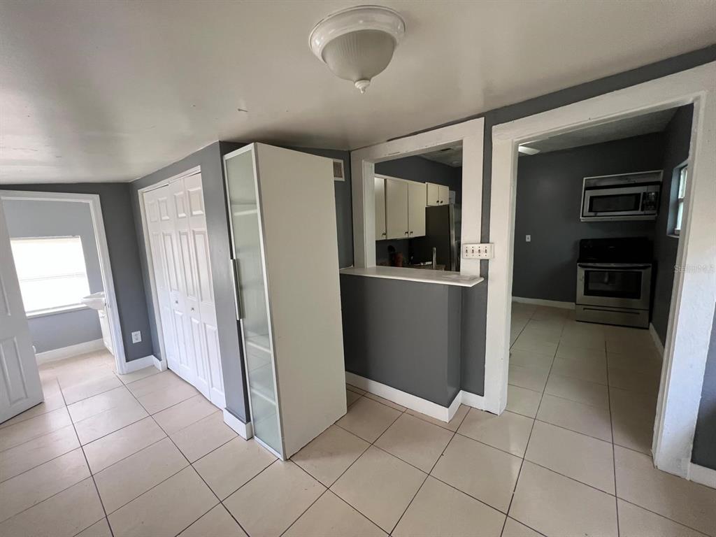 A room with tiled floors, a white storage cabinet, and a pass-through window to a kitchen — 1708 E NOME STREET, TAMPA, FL