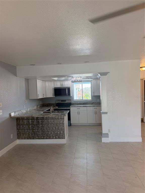 A kitchen features white cabinets, granite countertops, and a decorative metal-paneled breakfast bar — 2735 MAGDALINA DRIVE UNIT 2, PUNTA GORDA, FL