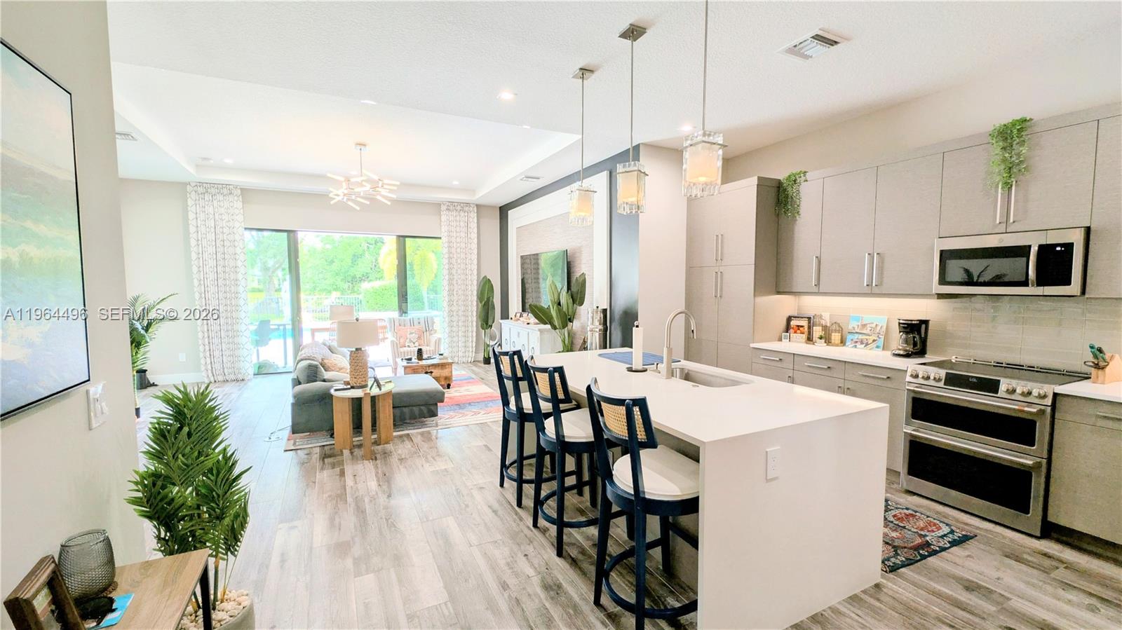 An open-concept kitchen and living area features a white island, gray cabinetry, and sliding doors — 2879 Gin Berry Way, West Palm Beach FL 33401, WEST PALM BEACH, FL