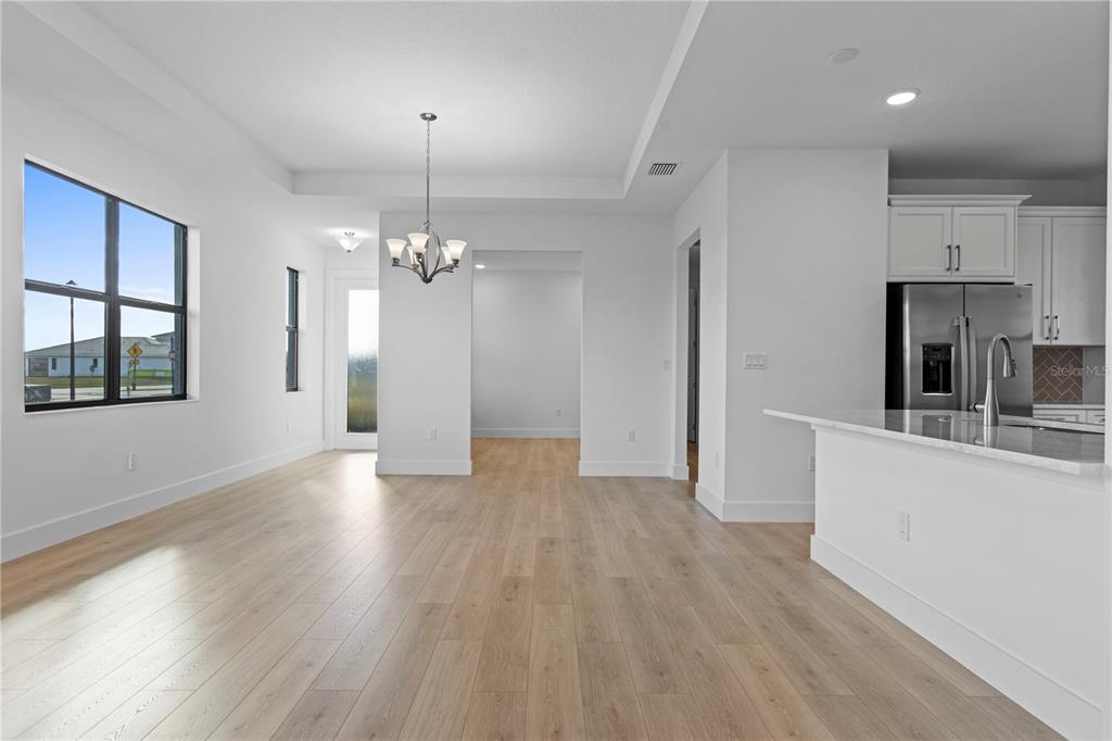 A bright dining area with light wood floors, a chandelier, and an adjacent kitchen — 18366 ROCKPORT PLACE, LAKEWOOD RANCH, FL