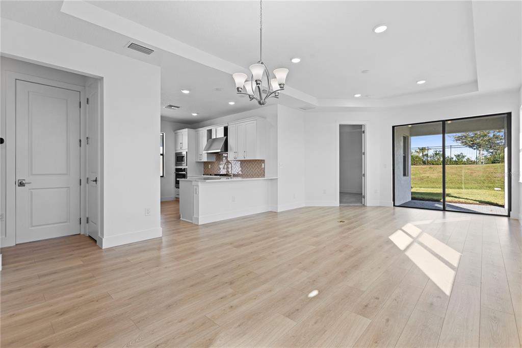 An open-concept living area features light wood flooring, a kitchen with white cabinetry, and sliding doors — 18366 ROCKPORT PLACE, LAKEWOOD RANCH, FL
