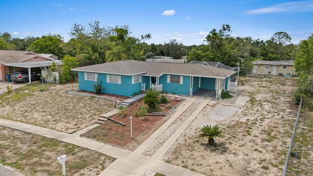 A bright blue single-story house features a front carport and a sandy, sparsely landscaped yard — 6495 FAIRLAWN STREET, SPRING HILL, FL