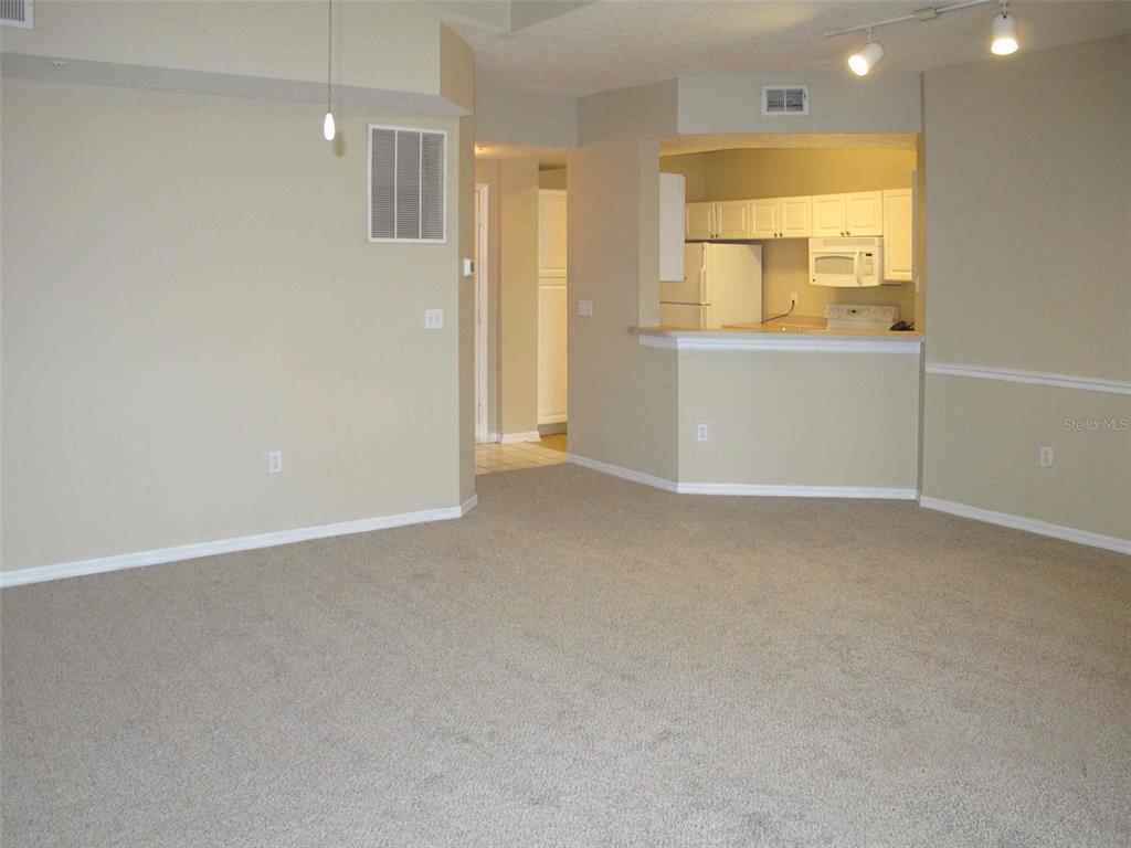 A carpeted living room opens to a kitchen with white cabinets and a breakfast bar — 5572 METROWEST BOULEVARD UNIT 310, ORLANDO, FL