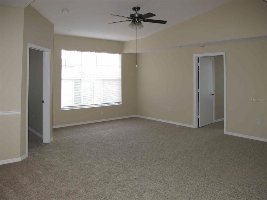 An empty bedroom features beige walls, tan carpeting, a ceiling fan, and two doorways — 5572 METROWEST BOULEVARD UNIT 310, ORLANDO, FL