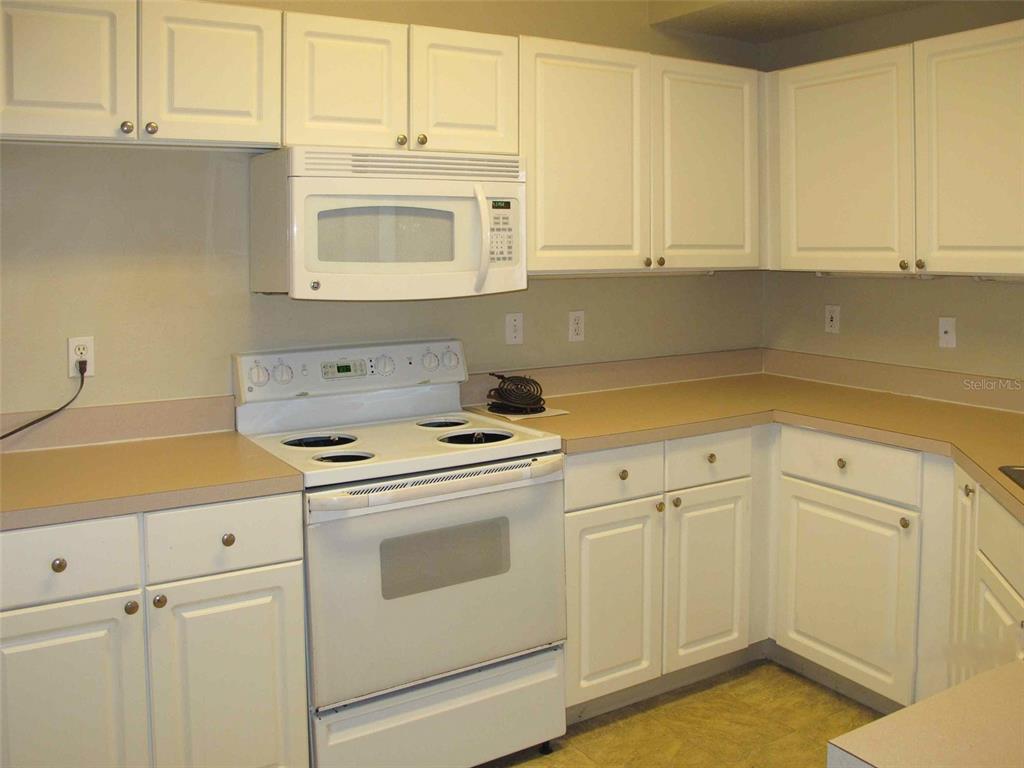 A kitchen features white cabinets, tan countertops, and white appliances including a range and microwave — 5572 METROWEST BOULEVARD UNIT 310, ORLANDO, FL