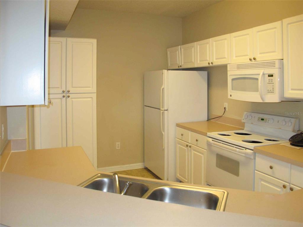 A kitchen features white cabinets, a white refrigerator, a white stove, and a double sink — 5572 METROWEST BOULEVARD UNIT 310, ORLANDO, FL