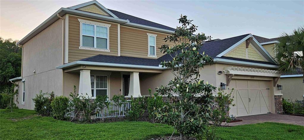 A two-story house with tan siding, a stone base, a front porch, and a garage — 13539 STANSIL AVENUE, ODESSA, FL