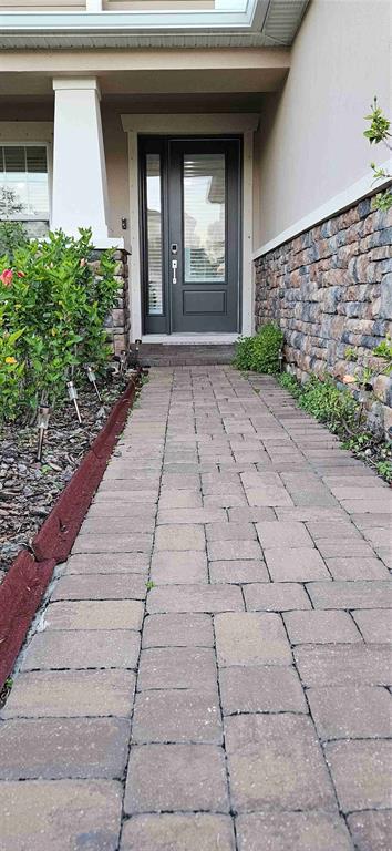 A paved walkway leads to a dark gray front door of a house with stone siding — 13539 STANSIL AVENUE, ODESSA, FL