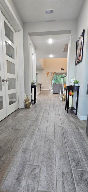 A hallway with gray wood-look tile flooring leads toward an open-concept living area — 13539 STANSIL AVENUE, ODESSA, FL