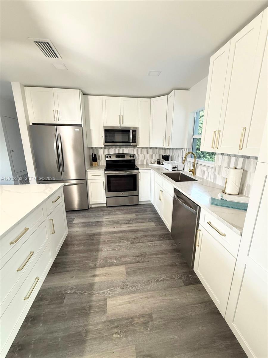 A modern kitchen features white cabinetry, stainless steel appliances, and wood-look flooring — 801 Broadhag Dr, Punta Gorda FL 33950, PUNTA GORDA, FL