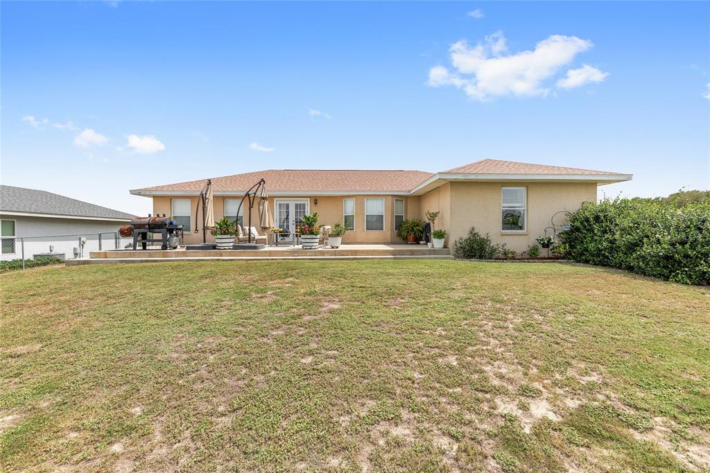 The back exterior of a single-story house features a concrete patio, lawn, and landscaping — 10057 SE 125TH STREET, BELLEVIEW, FL