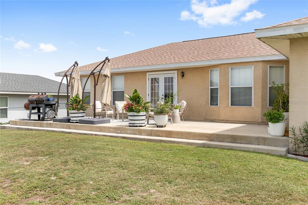 A tan stucco house features a concrete patio with outdoor furniture, potted plants, and umbrellas — 10057 SE 125TH STREET, BELLEVIEW, FL