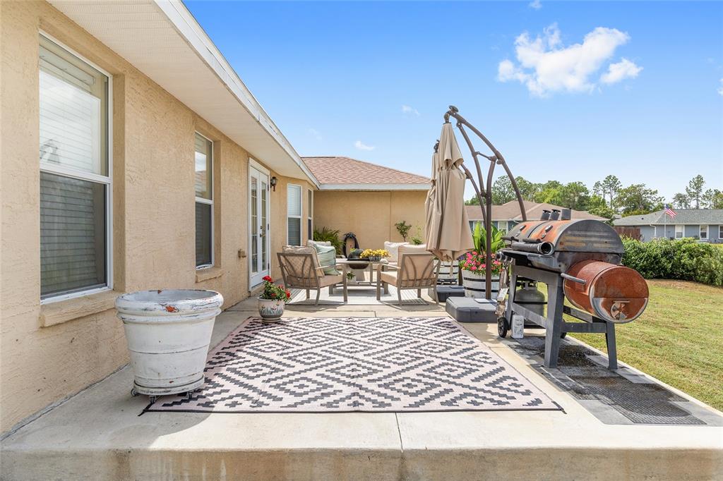 A concrete patio features a patterned rug, outdoor seating, a grill, and a large planter — 10057 SE 125TH STREET, BELLEVIEW, FL