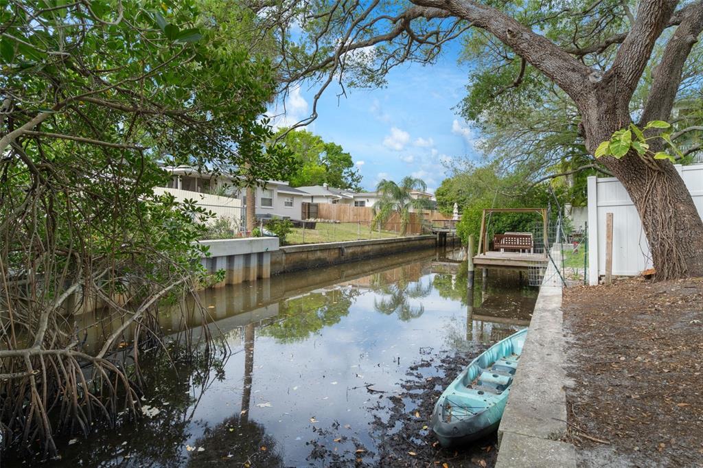 A backyard canal view featuring a small dock, a kayak, and mature trees — 4808 W EUCLID AVENUE, TAMPA, FL