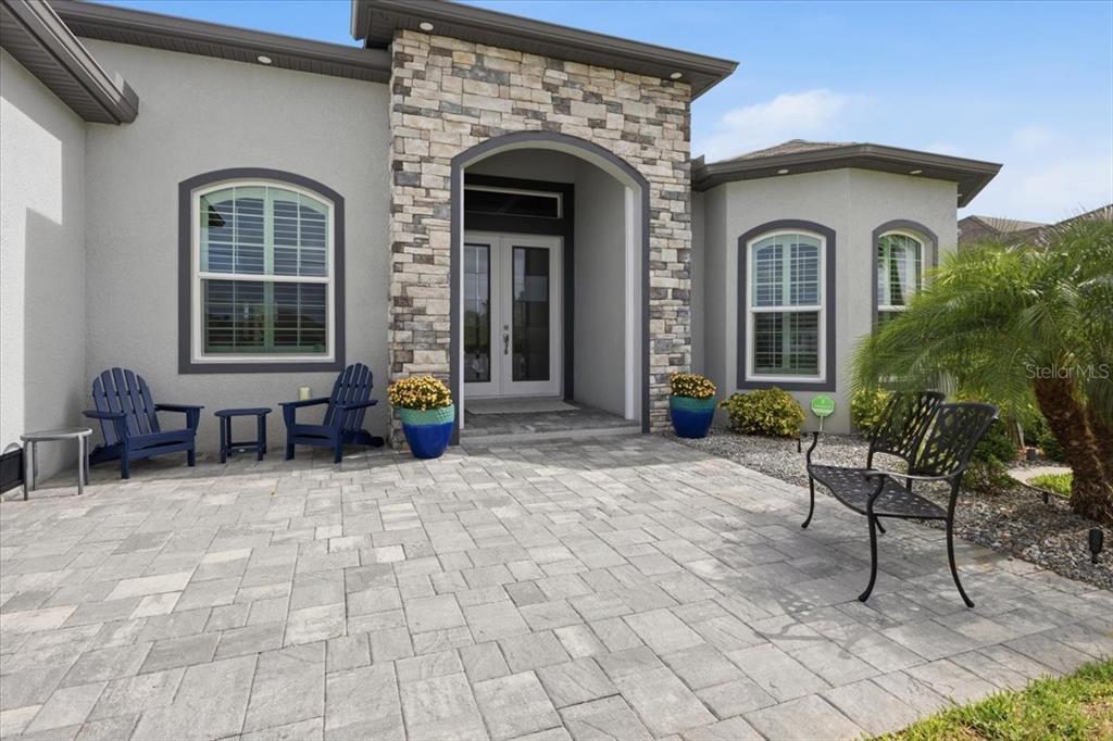 A stone-accented entryway features a paved patio with blue chairs and a metal bench — 9214 MELODY CIRCLE, PORT CHARLOTTE, FL