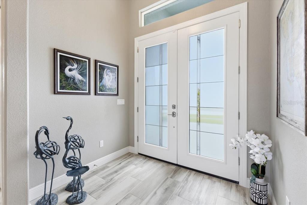 An entryway features double glass-paneled doors, light wood-look tile flooring, and decorative bird sculptures — 9214 MELODY CIRCLE, PORT CHARLOTTE, FL